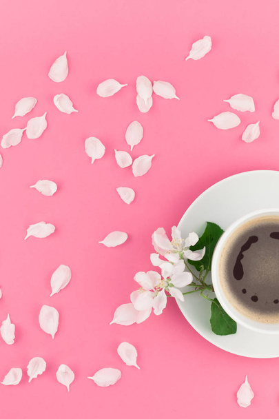 Δημιουργική επίπεδης lay έννοια κάτοψη του φλιτζάνι καφέ και λευκό δέντρο της apple λουλούδια πέταλα σε παστέλ ροζ φόντο με αντίγραφο χώρος σε minimal στυλ, πρότυπο για το κείμενο - Φωτογραφία, εικόνα
