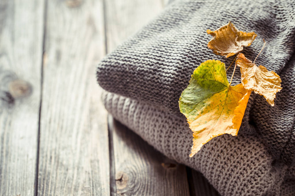 una pila de suéteres acogedores de punto y hojas de otoño sobre un fondo de madera
 - Foto, imagen