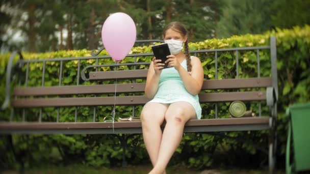 人工呼吸器でかわいい女の子がベンチの上の公園でタブレットを使用してください。 - 映像、動画