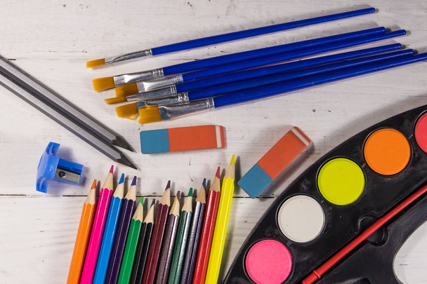 Set of drawing tools on white wooden background. Watercolor paints, paint brushes, color pencils, erasers and sharpener on desk. Top view - Photo, Image