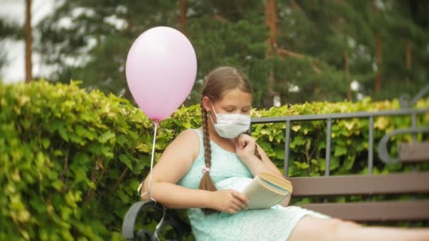 Roztomilá dívka v respirátor čtení knihy v parku na lavičce - Záběry, video
