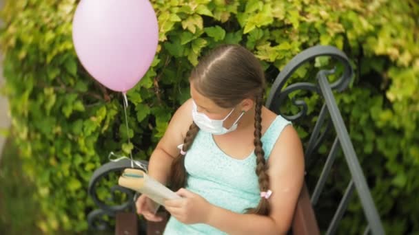 Menina bonito em um respirador lendo um livro no parque em um banco
 - Filmagem, Vídeo