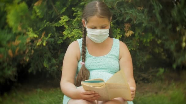 Roztomilá dívka v respirátor čtení knihy v parku na lavičce - Záběry, video