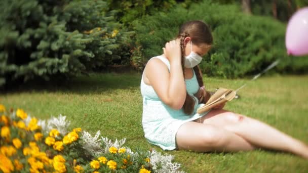 Cute girl in a respirator reading a book in the park - Filmati, video