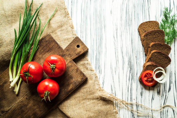 tomaten, groene uien, dille, Groenen, pasta, kwarteleitjes, brood op een bruin bord op een witte houten tafel - Foto, afbeelding