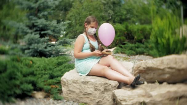 Menina bonito em um respirador lendo um livro no parque
 - Filmagem, Vídeo
