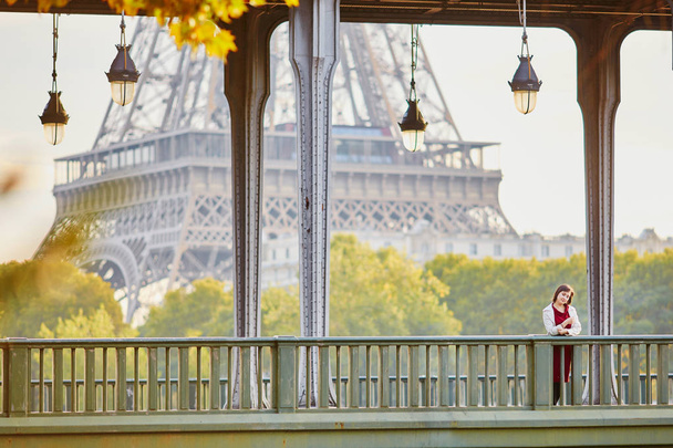 Beautiful young woman in Paris on Bir-Hakeim bridge with view to Eiffel tower on a fall or spring day. Tourism and vacation in France - 写真・画像
