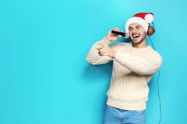 Young man in Santa hat singing into microphone on color background. Christmas music - Foto, immagini