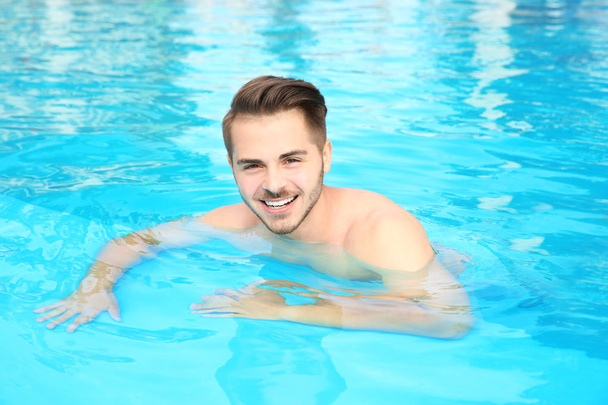 Young handsome man in swimming pool on sunny day - Φωτογραφία, εικόνα