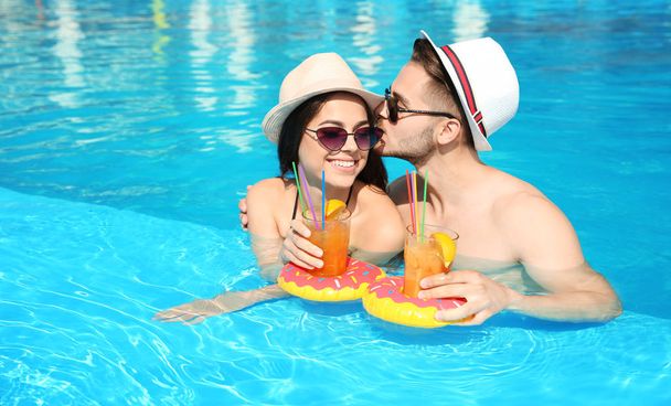 Young couple with refreshing cocktails in swimming pool on sunny day - Fotografie, Obrázek