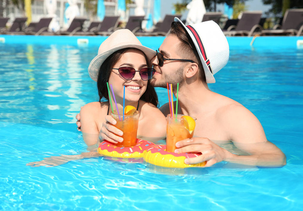 Young couple with refreshing cocktails in swimming pool on sunny day - Foto, immagini