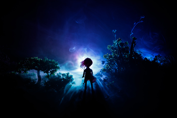 Horror Halloween decorato immagine concettuale. Una ragazza sola con la luce nella foresta di notte. Silhouette di ragazza in piedi tra gli alberi con luce surreale su sfondo. Focus selettivo
. - Foto, immagini