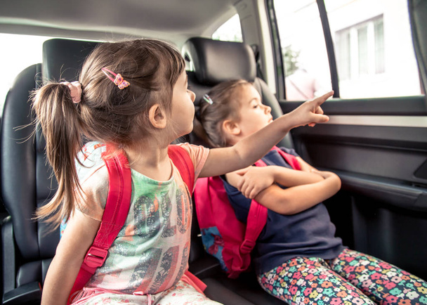 Dzieci w samochodzie iść do szkoły, szczęśliwy, słodkie twarze sióstr, uczniowie ze szkoły plecaki, siedząc w samochodzie rodzicielskiej przedszkola - Zdjęcie, obraz