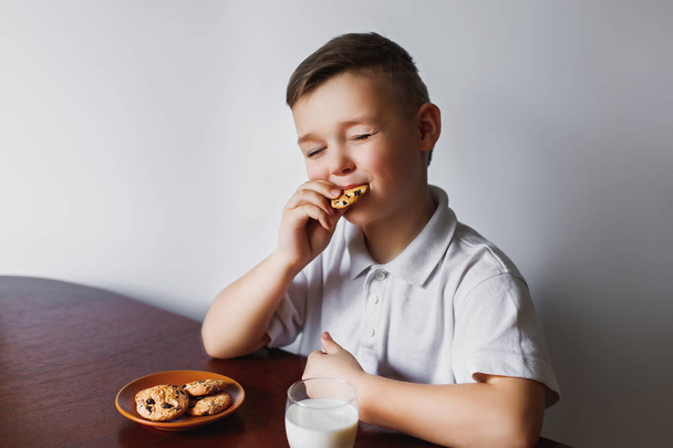 Een kleine jongen eet havermout koekjes en dranken met huisgemaakte melk. Gezond ontbijt opgesteld door mijn moeder. De schooljongen is ontbijten. - Foto, afbeelding
