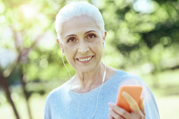 Cheerful elderly woman wearing earphones - Fotoğraf, Görsel