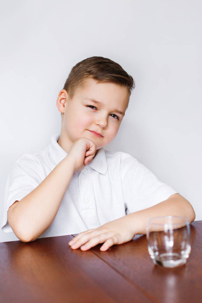 Młody chłopak siedzi przy stole w kuchni z pustej szklanki. - Zdjęcie, obraz
