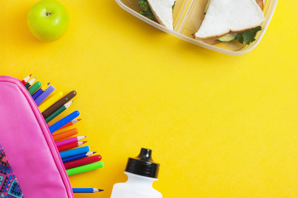 School lunch sandwich and green apple, bottle of water, healthy eating concept, colorful  pencils yellow background, copy space. - Photo, image