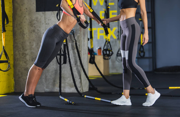 Woman instructor is assisting girl during TRX work out - 写真・画像