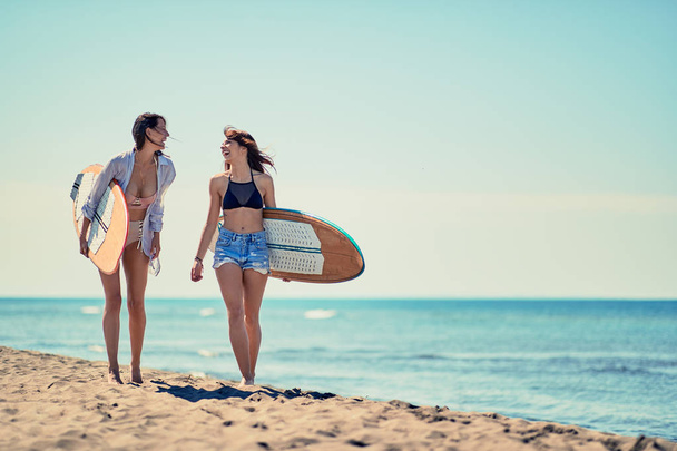 Surfers on beach having fun in summer. Young happy girls with a surf board on the beach - Фото, зображення