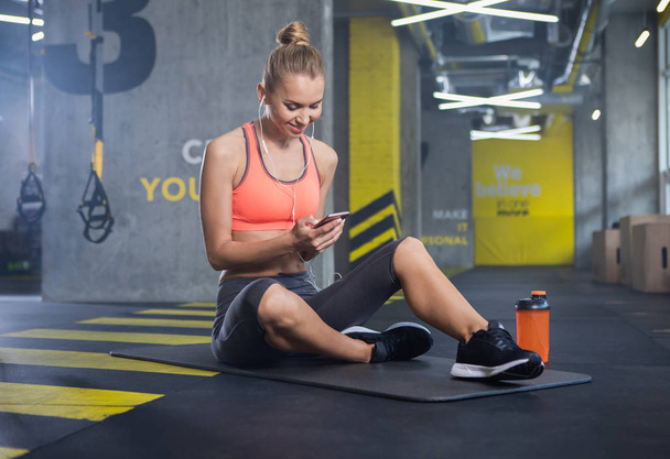 Happy woman is using smartphone during training indoors - 写真・画像