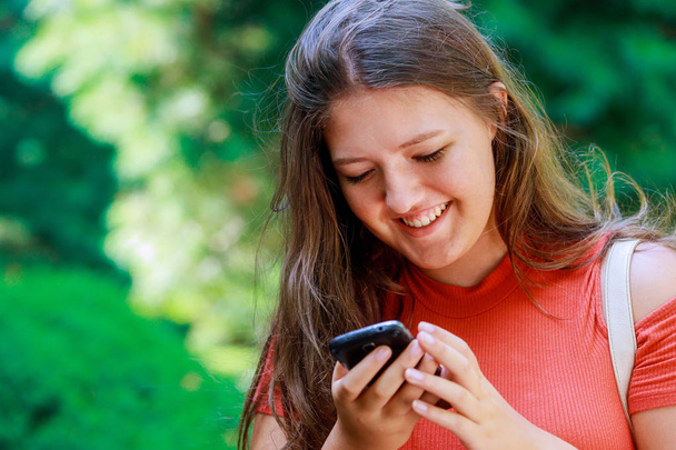 Усміхнена молода хороша дівчина-підліток читає повідомлення в соціальних мережах на мобільному телефоні
 - Фото, зображення