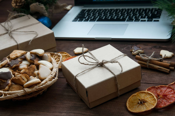 Lugar de trabajo de Navidad, cajas de regalo de Navidad, naranjas secas, canela y galletas de jengibre en una mesa de madera marrón con computadora
. - Foto, imagen