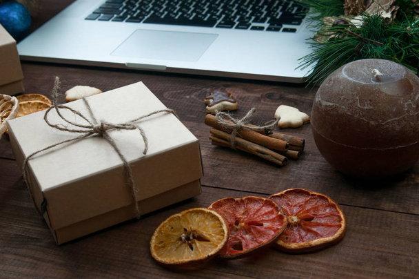 Kerst plaats kerst geschenkdozen, droge sinaasappels, kaneel en gember koekjes bezig met bruin houten tafel met computer. - Foto, afbeelding