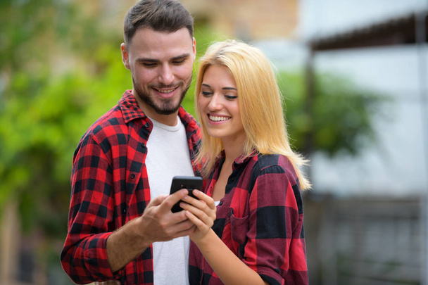 Young couple using phone together in the streets outdoors - Zdjęcie, obraz
