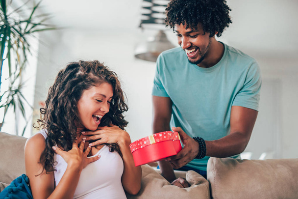 African man giving red surprise gift to woman at home - Fotó, kép
