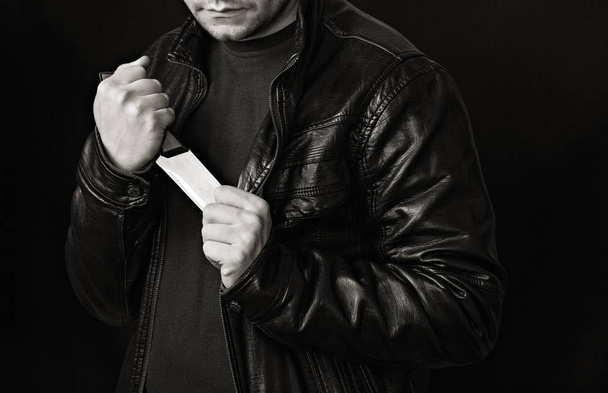 A man takes a knife out of a jacket, a black background, black and white - Φωτογραφία, εικόνα