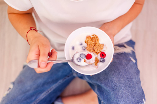 A woman is eating yogurt with cereal and berries for breakfast, holding a spoon, close-up hands, a healthy diet and a diet concept, summer berries - Foto, Imagem