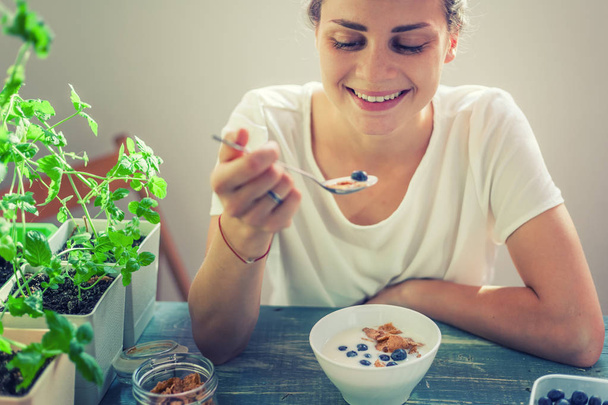 Young beautiful girl woman eating yogurt with flakes and berries for breakfast, healthy food, summer berries, diet - Zdjęcie, obraz