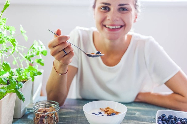 Young beautiful girl woman eating yogurt with flakes and berries for breakfast, healthy food, summer berries, diet - Photo, Image