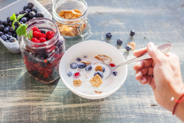 A woman is eating yogurt with cereal and berries for breakfast, holding a spoon, close-up hands, a healthy diet and a diet concept, summer berries - Foto, Bild