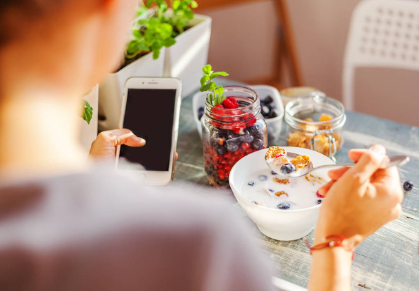 Healthy breakfast and social networks, girl's hands close up, yogurt with cereal and fresh berries, healthy eating concept and calorie counting - Foto, Bild
