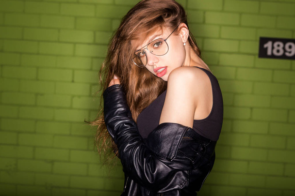 Fashion studio hard flash portrait of beautiful young pretty lady in fashion glasses, rock black style leather jacket look to camera. Hipster urban style girl. Lifestyle outdoor city portrait. - Фото, изображение