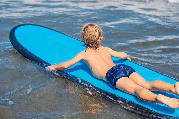 Happy baby boy - young surfer ride on surfboard with fun on sea waves. Active family lifestyle, kids outdoor water sport lessons and swimming activity in surf camp. Summer vacation with child. - Photo, Image