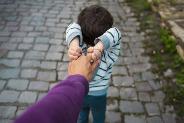 Мальчик тянет руку своего отца. Папа гуляет с сыном по городской улице. Ребенок капризен и не отпускает руку родителя
. - Фото, изображение