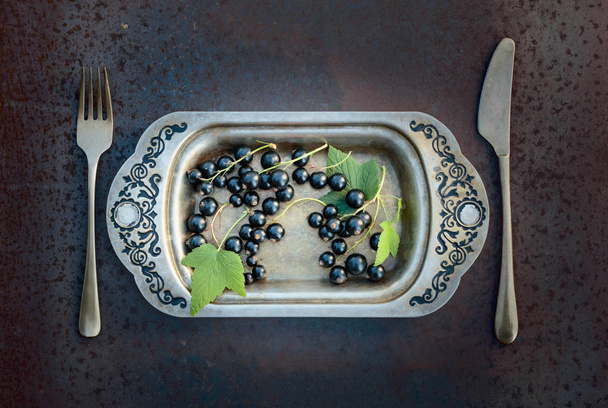 Ribes nero su un piatto di metallo con forchetta e coltello. Concetto per un'alimentazione sana, dieta e antiossidante
. - Foto, immagini