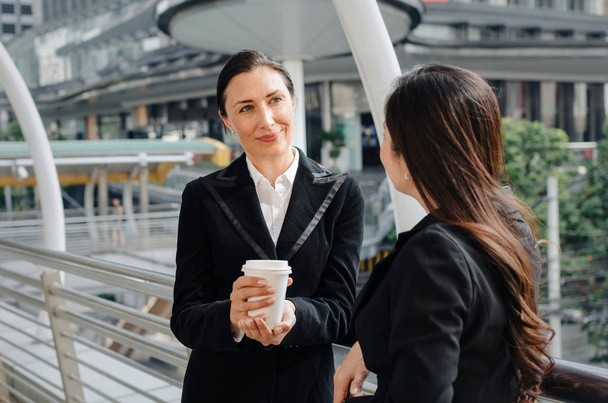 two business asian and caucasian woman with coffee cup talking about finance news together in the modern city, congratulation, success, meeting, partner, teamwork, community and connection concept - Foto, Imagem
