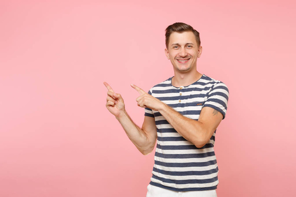 Portrait excited smiling young man wearing striped t-shirt pointing index fingers aside on copy space isolated on trending pink background. People sincere emotions lifestyle concept. Advertising area - Foto, Imagen