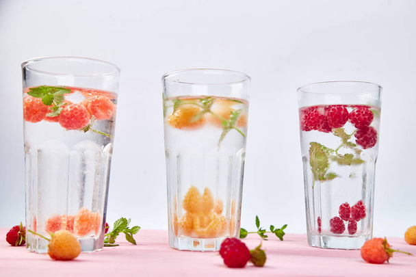Detox infused flavored water with three color raspberry - red, orange, yellow on pink background.. Refreshing summer homemade cocktai - Foto, Imagen