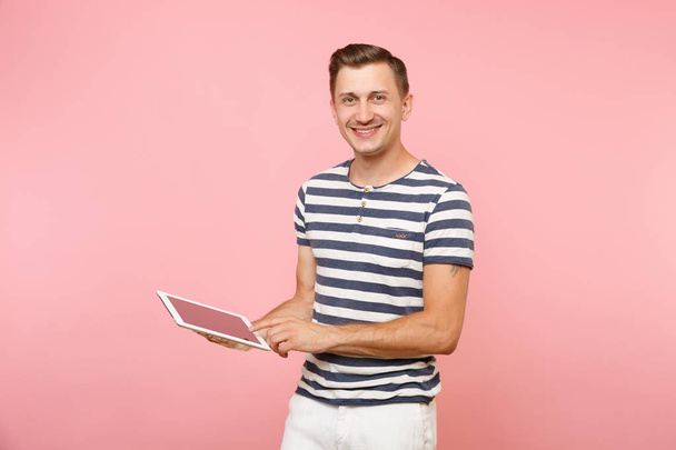 Portrait de jeune homme utilisateur portant un t-shirt rayé travaillant sur tablette PC isolé sur fond rose pastel tendance. Les gens sincères émotions concept de style de vie. Espace publicitaire sur l'espace de copie
 - Photo, image