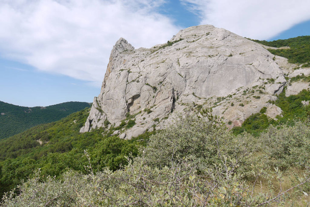 El pico de la montaña rocosa contra el telón de fondo de los bosques verdes suaves y el cielo azul sin fin
 - Foto, Imagen