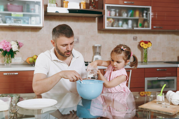 Dziecko dziewczynka pomaga człowiekowi gotować ciasteczka świąteczne imbir, wlać mąkę do miski, przy stole. Szczęśliwa rodzina tata, córka dziecko gotowanie żywności w weekend rano. Wakacyjny dzień ojca. Dzieciństwa rodzicielstwa - Zdjęcie, obraz