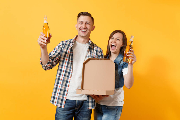 Молодые счастливые счастливые пара женщина и мужчина спортивные болельщики подбодрить команду поддержки держать бутылки пива и итальянскую пиццу в картонной плоской коробке изолированы на желтом фоне. Концепция семейного отдыха
 - Фото, изображение