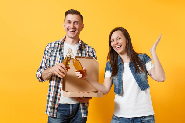 Nuori iloinen pari nainen mies urheilu tuuletin piristää tukitiimi clinking olutpulloja pidä italialaista pizzaa pahvi flat box levitä kädet eristetty keltaisella taustalla. Urheilu perheen vapaa-ajan elämäntapa
 - Valokuva, kuva