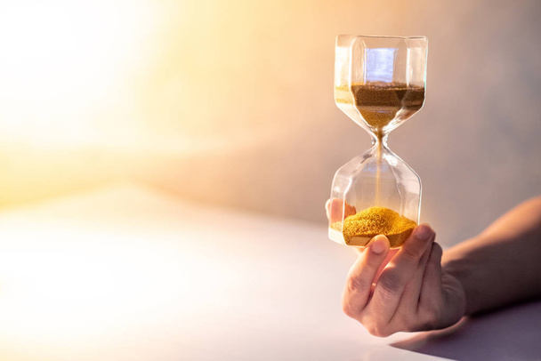 Close up of gold sand running through the shape of modern hourglass on male hand.Time passing and running out of time. Urgency countdown timer for business deadline concept with copy space - Fotoğraf, Görsel