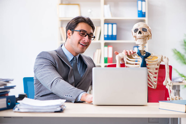 Бизнесмен, работающий со скелетом в офисе - Фото, изображение