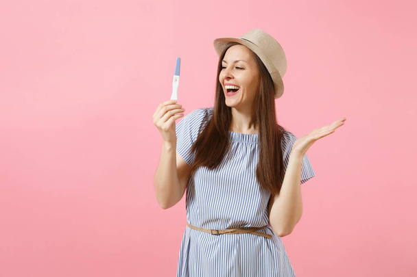 Excited happy woman in blue dress, hat hold in hand, looking at pregnancy test isolated on pink background. Medical healthcare gynecological, pregnancy fertility maternity people concept. Copy space - Φωτογραφία, εικόνα